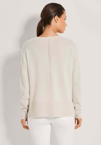 Hellbeige oversized Pullover mit langen Ärmeln, geripptem Saum und vertikalem Strickdetail entlang des Rückens. Weicher Griff, lässige Passform.