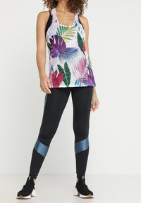 Mönstrad tanktop i flera färger med blommönster och randig bakgrund, matchad med svarta leggings med blåa accentstripes och texturerade sneakers.