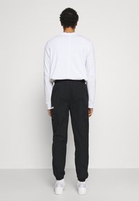 Vitt långärmat skjorta och svarta cargobyxor med elastiska muddar, utrustade med sidofickor och en minimalistisk design, tillsammans med vita sneakers.