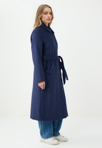 Marineblauwe wollen jas met een dubbelzijdig ontwerp, grote knopen en een tailleband, met een hoge kraag en lange mouwen.