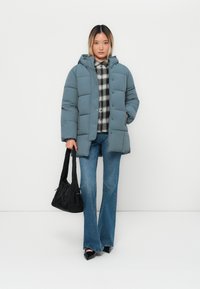 Piepūšams zils žakets ar kapuci, ar spiedpogām, uzvilkts virs melna un baltā rūtainā krekliņa. Saskaņots ar flared džinsiem un melnu somu.