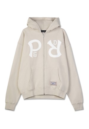 Beige zip-up hoodie made of soft material, featuring a large white logo on the chest, front pockets, and a drawstring hood.
