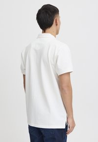 Hvit kortermet polo skjorte med myk tekstur, klassisk krage og sideslisser. Enkelt design uten mønstre eller detaljer.