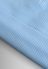 Svetlomodrá rebrovaná pletená tkanina s mäkkou textúrou, obsahujúca diagonálny záhyb, ktorý ukazuje dizajn a vlastnosti materiálu.