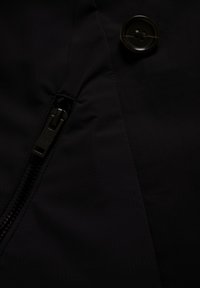 Tela negra con una cremallera negra cerrada a la izquierda y un gran botón negro cosido en el lado derecho.