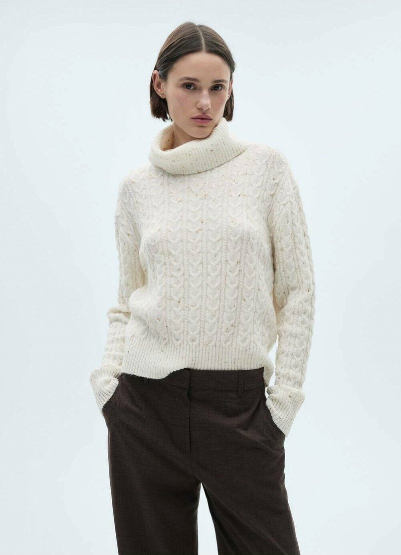 Cream-colored knitted sweater with a high collar, featuring a textured cable pattern and ribbed cuffs, paired with dark brown trousers.