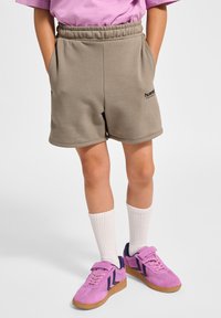 Ljust beige svettshorts med elastisk midja och sidofickor. Matcher med rosa sneakers med marinblå detaljer och vita ankelsockor.