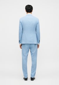 Σετ ανοιχτό μπλε κοστούμι που περιλαμβάνει σακάκι με ραφή στα μέτρα και ταιριαστό παντελόνι. Το ύφασμα έχει διακριτή υφή, με κούμπωμα με ένα κουμπί και στενή εφαρμογή.