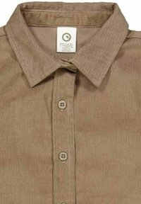 Bruine corduroy shirt met een kraag, knopen aan de voorkant en een label met de merknaam mūsli. De stof heeft een gestructureerd streepjespatroon.