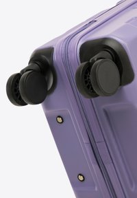 Valise rigide violette avec une surface texturée, deux roues noires et une fermeture éclair. Comprend des accents noirs et des rivets en métal.