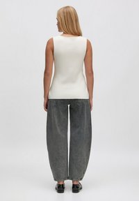 Weißes ärmelloses Oberteil in einer taillierten Passform, kombiniert mit lockeren, dunkelgrauen, weiten Jeans. Der Look wird mit schwarzen Schuhen abgerundet.