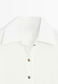 Camicia bianca con colletto classico, dotata di cinque bottoni rotondi e texture, e un piccolo accento dorato vicino allo scollo.