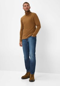 Maglione a dolcevita marrone, maniche lunghe, design aderente; abbinato a jeans blu a gamba dritta e stivaletti marroni con lacci.