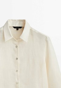 Light beige linen shirt with a classic collar, featuring a buttoned placket and transparent buttons. Smooth texture and long sleeves.