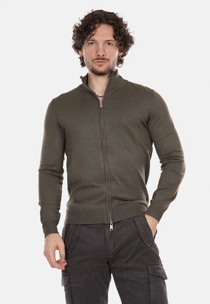 Pullover verde oliva con cerniera, caratterizzato da una texture a coste e colletto alto. Presenta una cerniera in metallo e una vestibilità aderente ai polsini e in vita.