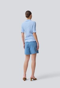 Top tricotado azul claro texturizado com mangas curtas e bainha em scallop, combinado com calções de ganga azuis e mules de salto bloco em tom de caramelo.