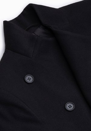 Cappotto di lana nera con colletto appuntito, design doppiopetto e tessuto testurizzato, accentuato da due grandi bottoni neri.