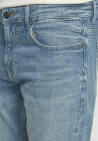 Jeans en denim bleu clair avec une finition légèrement délavée. Comprend des poches avant, des passants de ceinture et des coutures contrastées.