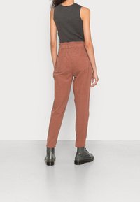 Kalhoty z lněné směsi v rustikální barvě s elastickým pasem a dvěma zadními kapsami. Zúžené nohavice a textilní struktura s vráskami. Stylizováno s černými botami.