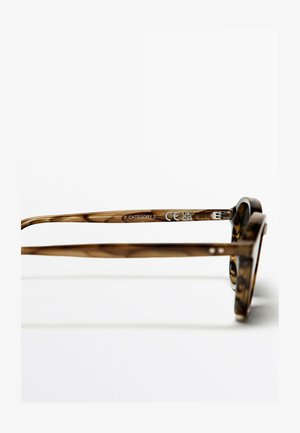 Bruine schildpadzonnebril met een robuust montuur, platte pootjes en tekst "P CATEGORY 3" op de binnenkant van het montuur.