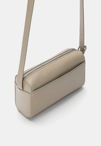 Sac bandoulière rectangulaire en cuir beige avec une texture lisse, doté d'une fermeture éclair, d'une sangle ajustable et de détails de couture discrets.