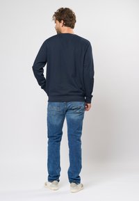 Pantalon lung cu maneci de marine, asortat cu blugi decolorati. Această ținută are un croi casual, cu manșete și tiv cu nervuri.