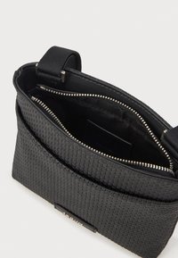 Μαύρη υφασμάτινη τσάντα με λείες εσωτερικές επενδύσεις, κλείσιμο με φερμουάρ και ανθεκτική λαβή; διαθέτει επίπεδη εξωτερική τσέπη και μεταλλικά στοιχεία.