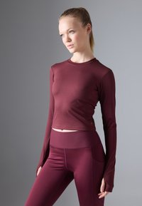 Burgundy long-sleeve top with a fitted design and ribbed hem, paired with matching high-waisted leggings featuring side pockets.