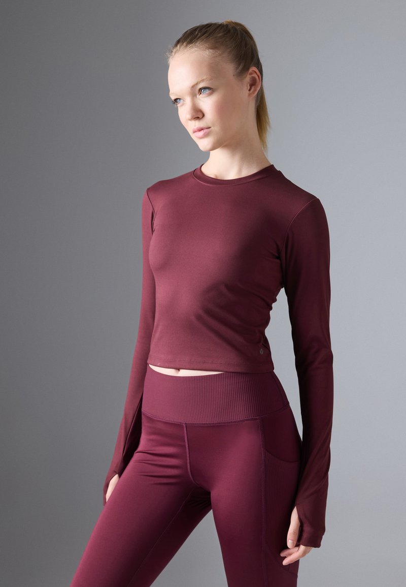 Burgundy long-sleeve top with a fitted design and ribbed hem, paired with matching high-waisted leggings featuring side pockets.