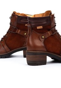 Brown leather and suede ankle boots with a lace-up design, metallic accents, and a stacked heel featuring textured rubber soles.