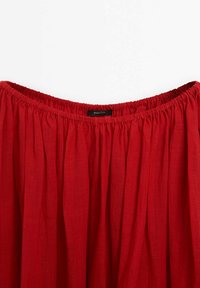 Jupe rouge froncée avec taille élastique et étiquette de marque visible au centre du dos, fabriquée en tissu léger.