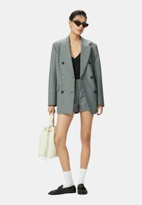 Blazer de cuadros gris de doble botonadura con pantalones cortos a juego. El modelo lleva un bolso blanco tipo cubo y usa planos negros y calcetines blancos de caña corta.