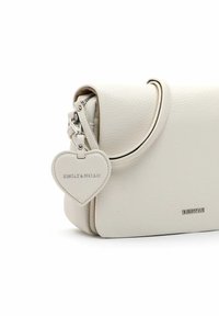 Weiße Lederhandtasche in runder Form, ausgestattet mit einem silbernen herzförmigen Anhänger und einem dezenten Logo. Texturierte Außenseite, minimalistisches Design.