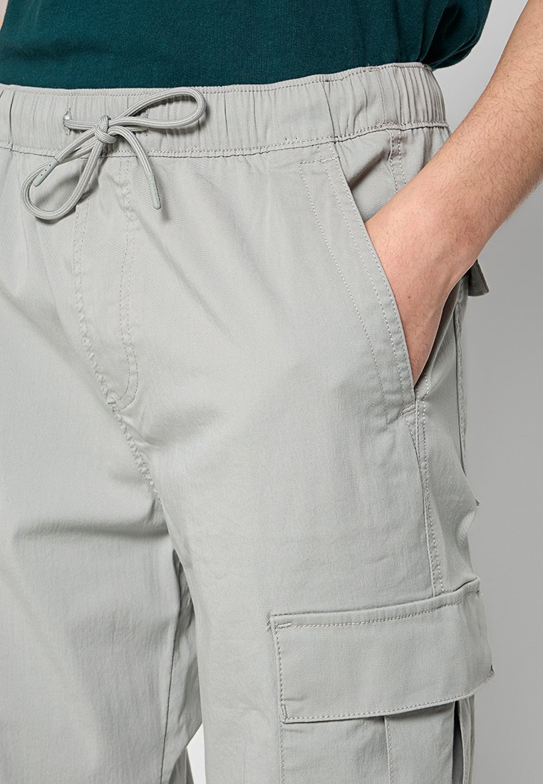Hellgraue Cargo-Hosen aus weichem Stoff, mit einem elastischen Bund und Kordelzug, seitlichen Taschen und einer aufgesetzten Tasche am Oberschenkel.