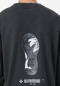 Black cotton sweatshirt featuring a large graphic of a shoe print on the back, with white text and details below the print.