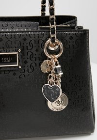 Sac à main noir en synthétique avec un motif de logo en relief, quincaillerie dorée, anse tressée et plusieurs accents de charme, y compris une forme de cœur.