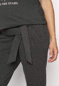 Grå sweatshirt med korta ärmar och en grafisk design. Mörkgrå byxor med en tygbälte knutet i midjan, slät textur.