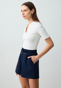 Witte geribbelde T-shirt met korte mouwen en gekartelde randen, gecombineerd met marineblauwe shorts met een elastische tailleband en zijzakken.