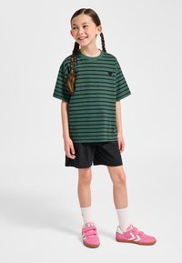 Grönrandig kortärmad t-shirt med en svart logotyp, kombinerad med svarta shorts och rosa kardborreskor med vita detaljer och vita strumpor.