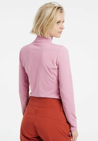 Top a maniche lunghe di colore rosa chiaro con colletto alto, design aderente e texture liscia, abbinato a pantaloni color ruggine con tasche.