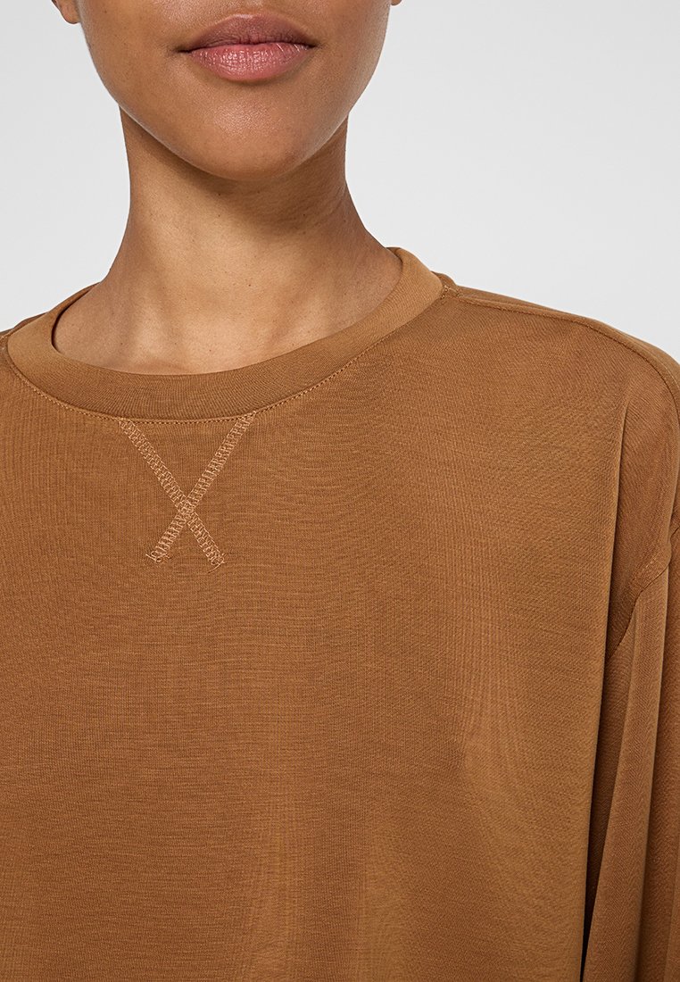 Bruine overhemd met lange mouwen, voorzien van een brede ronde halslijn en een gestructureerde stiksel detail op de borst in de vorm van een 'X.' Gladde stof.