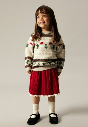 Maglione lavorato a maglia con motivi festivi, inclusi volti di Babbo Natale e alberi. Una gonna rossa a pieghe con orlo a scallop, abbinata a calze bianche e scarpe nere.