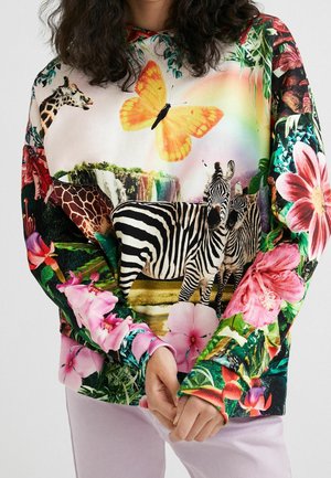 Sweat-shirt avec imprimé animalier vibrant présentant des zèbres, une girafe, un grand papillon orange, une cascade et des fleurs tropicales colorées sur les manches.