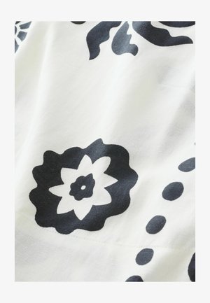 Sort blomstermønster på et hvidt stof, med markante kronblade og cirkulære detaljer, og en glat, let tekstureret overflade.