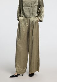 Olive green, lightweight fabric top with long sleeves paired with wide-leg, pleated trousers in the same shade; black pointed heels.