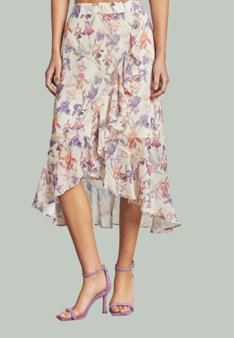 Falda midi floral con dobladillo asimétrico, con colores pastel y bordes con volantes. Combinada con sandalias de tacón ligeras de color púrpura. Textura de tela suave.