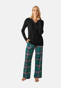 Musta pitkähihainen paita, jossa on napit, ja vihreät ruudulliset housut, joissa on vaaleanpunaisia ja valkoisia viivoja. Pehmeä kangas, rento istuvuus ja leveät lahkeet.