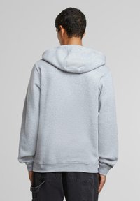 Grå sweatshirt med hette, snor, ribbete mansjetter og hem, og en teksturert overflate, sett bakfra.