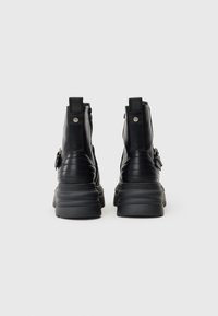 Μαύρες δερμάτινες μπότες μέχρι τον αστράγαλο με χοντρή σόλα, πλαϊνούς φερμουάρ και λεπτομέρειες από λουριά. Υφή στην πλάτη και επενδυμένη λεπτομέρεια στον γιακά.