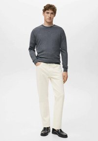 Suéter de punto gris, pantalones color crema y mocasines negros. El conjunto presenta texturas suaves y un ajuste relajado, con un diseño sencillo.
